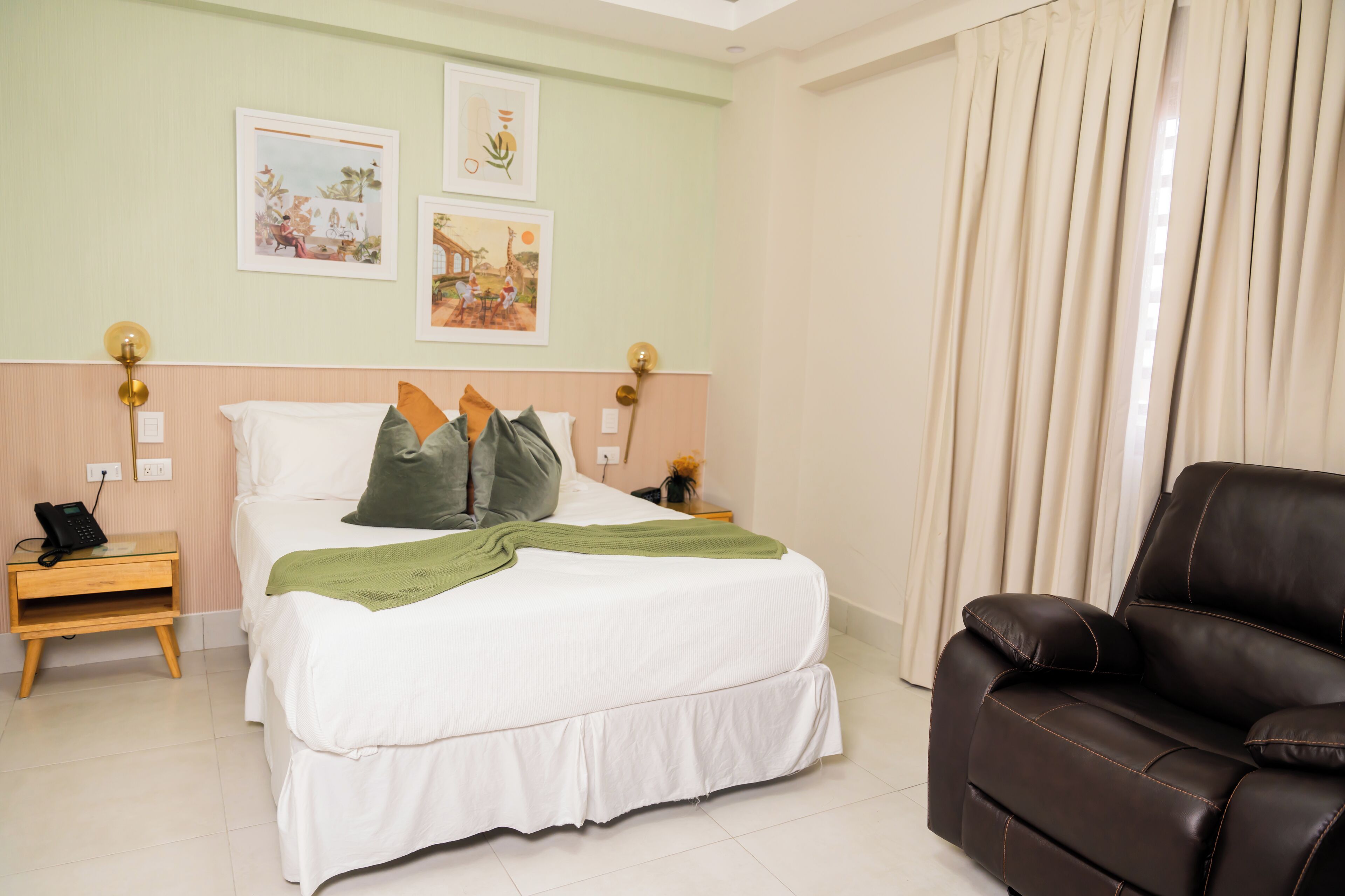 Habitación de hotel con cama, mesita de noche con teléfono, sofá de cuero marrón y dos lámparas de pared.