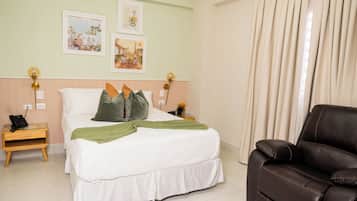 Habitación de hotel con cama, mesita de noche con teléfono, sofá de cuero marrón y dos lámparas de pared.