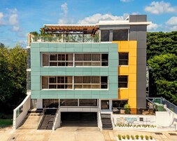 Un hotel moderno de varios pisos con techo plano, ventanas amplias y un letrero que dice 'STAY HERE Suites'.