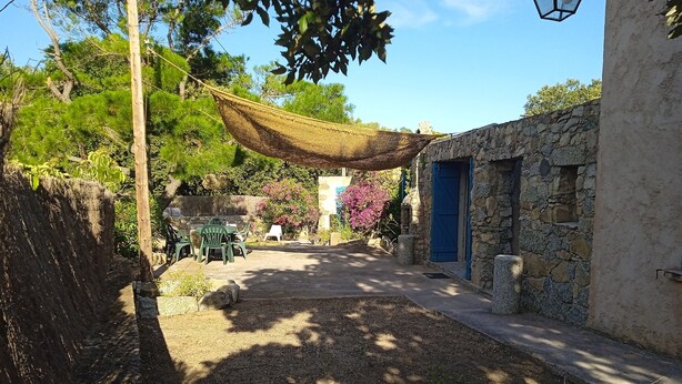 Un espacio al aire libre rústico con un muro de piedra, una puerta azul y una hamaca.