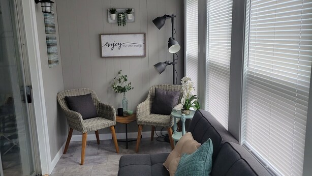 Un salon moderne avec un canapé gris, des fauteuils en osier et une petite table agrémentée de plantes.