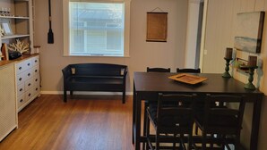 Un coin repas comprenant une table et des chaises en bois, un banc, une bibliothèque et une fenêtre avec des stores.