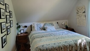 Une chambre à coucher bien rangée, avec un lit, des tables de chevet, une décoration murale en macramé et des tableaux encadrés.