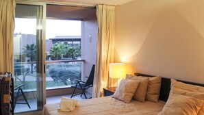 A hotel room with a bed, a chair, a lamp, and a view of the outside. - Herdade dos Salgados, T3 8D-0B, Vila das Lagoas (Albufeira)