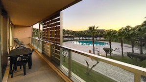 A balcony with a view of a pool area, including a circular pool and palm trees. - Herdade dos Salgados, T3 8C-1B, Vila das Lagoas (Albufeira)