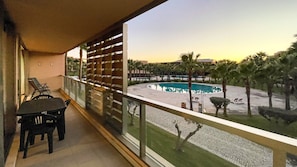 A balcony with a view of a pool area, including a circular pool and palm trees. - Herdade dos Salgados, T3 8C-1B, Vila das Lagoas (Albufeira)