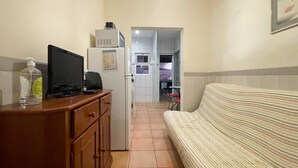 Une chambre d’hôtel compacte comprenant un coin cuisine, une commode en bois, un téléviseur et un canapé à rayures.