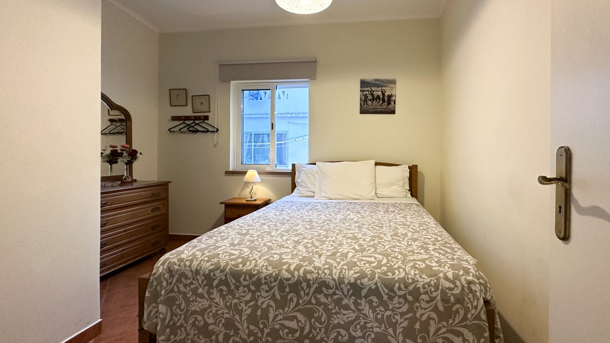 Ein Schlafzimmer mit Bett, Schminktisch, Nachttisch, Lampe, Fenster und Kunstwerk.