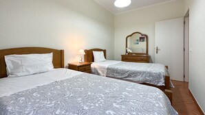 Hotellihuone, jossa on kaksi sänkyä, yöpöytä lampun kanssa, lipasto ja peili.