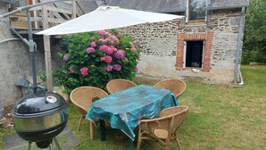 Eine Terrasse mit Tisch, Stühlen, einem Grill und einem weißen Sonnenschirm.