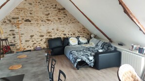 Ein gemütliches Schlafzimmer im Dachgeschoss mit Steinwand, einem Bett mit gemusterten Textilien, einem Esstisch mit Stühlen und Holzboden.