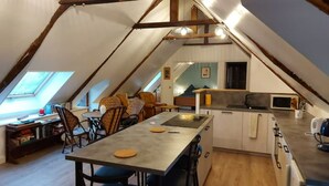 Ein gemütliches Schlafzimmer im Dachgeschoss mit schrägen Wänden, einer kleinen Küchenzeile und einer Essecke mit Tisch und Stühlen.