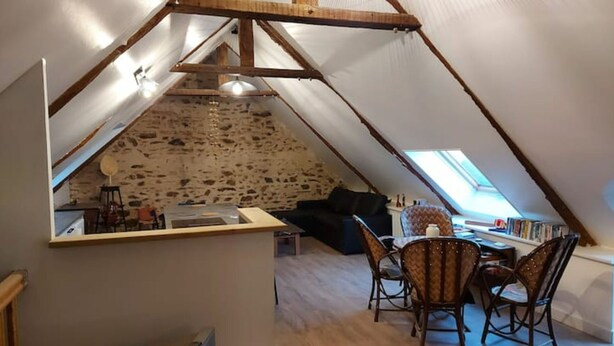 Ein gemütlicher Dachraum mit einer Steinwand, einer Essecke mit Stühlen und einem Bücherregal.