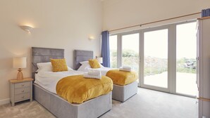 A modern bedroom with two beds, a nightstand, and a large window with a view. - Luxury 2-Bed Cotswolds Barn with Private Hot Tub | Sleeps 4 (Gloucester)