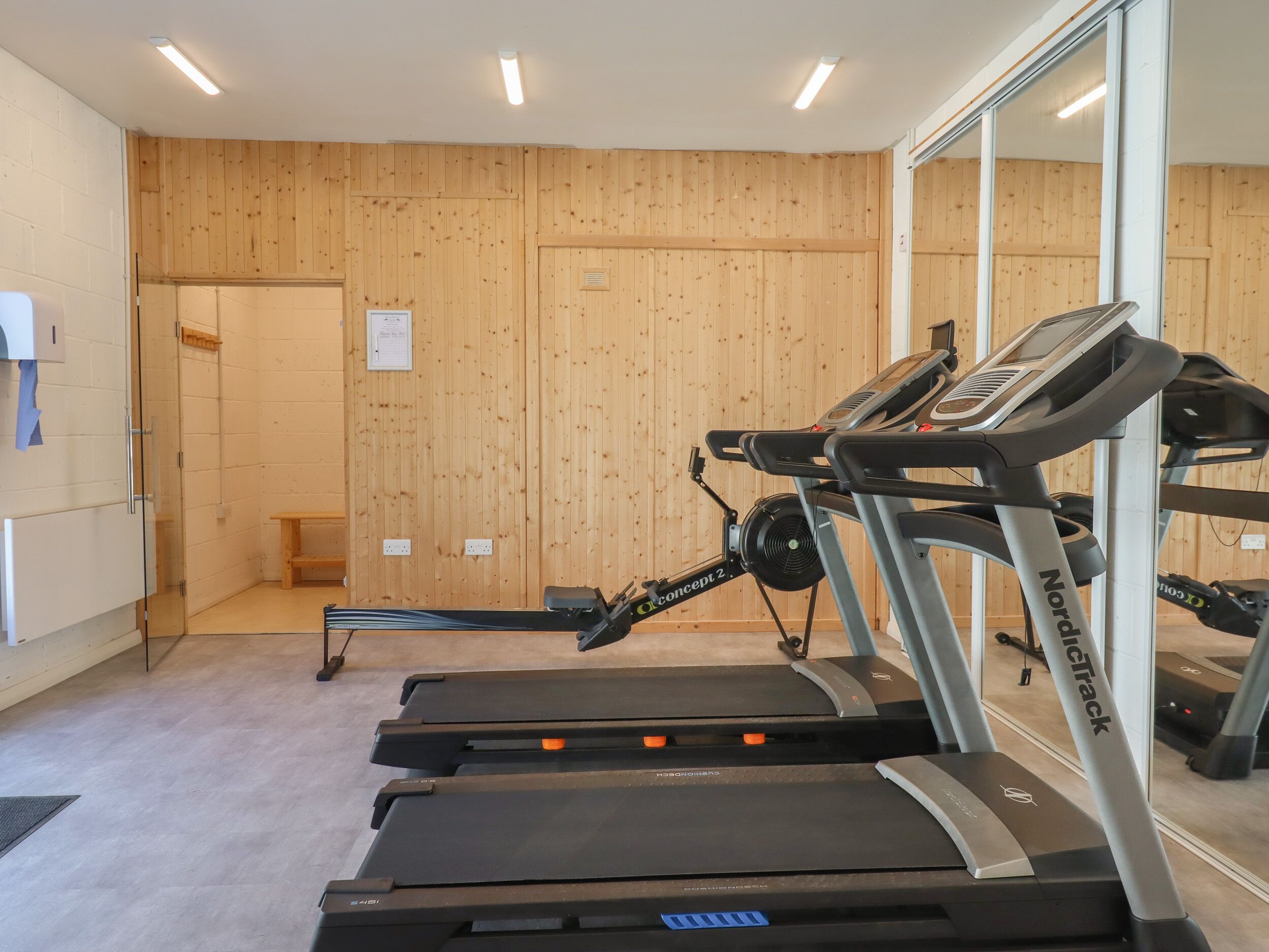 A gym with treadmills, a wooden wall, a mirror, and a small bench.