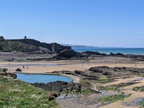 A coastal landscape with rocky terrain, a beach, and a clear sky. - Strawberry Bank - Nuthatch (Holsworthy)