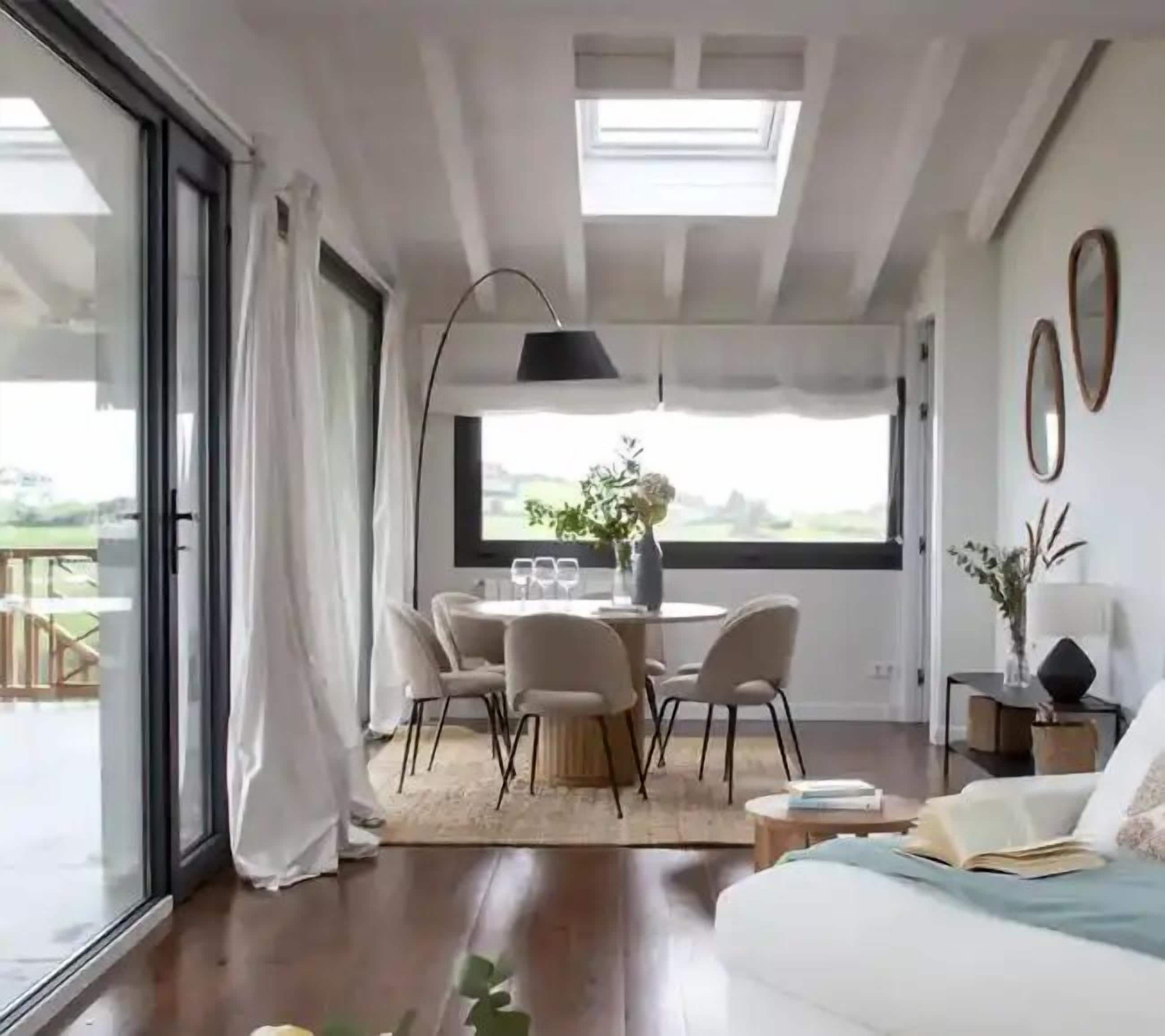 A modern living room with a dining area, large windows, and a view of the outdoors.