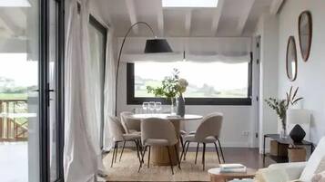 A modern living room with a dining area, large windows, and a view of the outdoors.