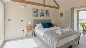 A bedroom with a large bed, two bedside tables, a headboard, and a view of the outdoors.