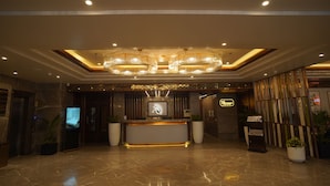 A hotel lobby with a reception desk, large potted plants, and a modern chandelier. - Hotel Apricia  (Ludhiana)