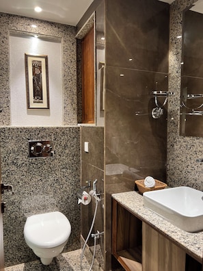 Un baño moderno con encimera de granito, un lavamanos blanco y zona de ducha.