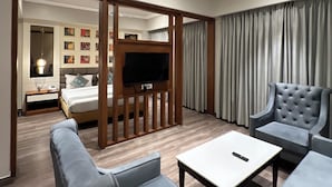 A modern living room with a sofa, armchairs, a coffee table, a TV, and a ceiling fan. - Hotel Apricia  (Ludhiana)