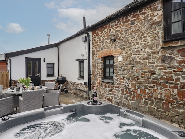 A stone building with a hot tub, outdoor seating, and a grill.