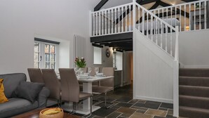 A spacious living area with a dining table set for six, a grey sofa, and a staircase leading to an upper level. - Strawberry Bank - Pipistrelle (Holsworthy)