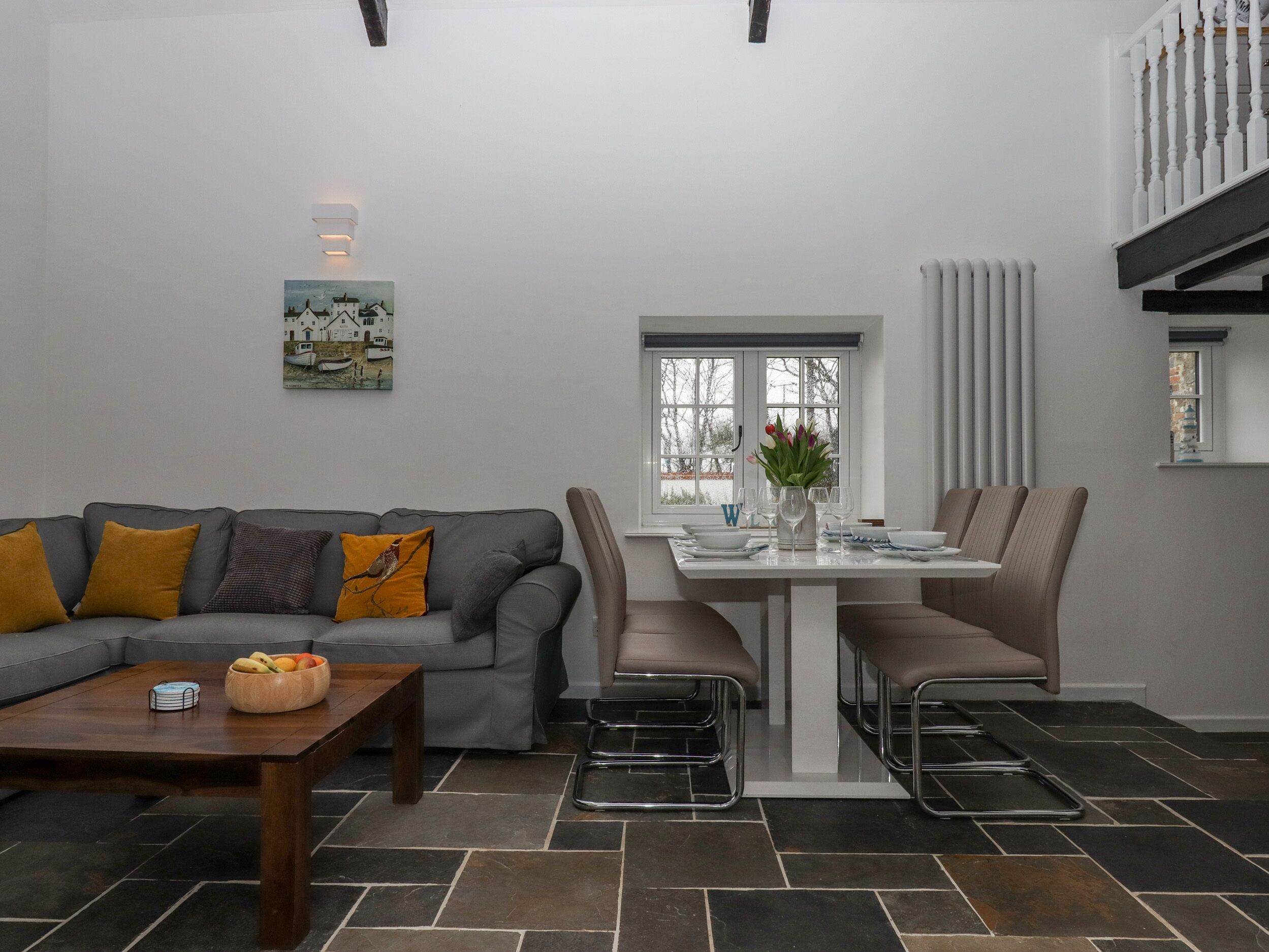 A modern living room with a grey sofa, a wooden coffee table, and a dining area with a white table and chairs.
