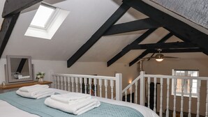 A bedroom with a sloped ceiling, a bed with white linens and a teal blanket, a wooden dresser, a mirror, and a window with a view of the outside. - Strawberry Bank - Pipistrelle (Holsworthy)