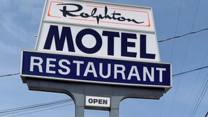 Ein Schild mit der Aufschrift 'Ralphton', einem Motel und Restaurant, und darunter ein 'ÖFFNEN'-Hinweis.