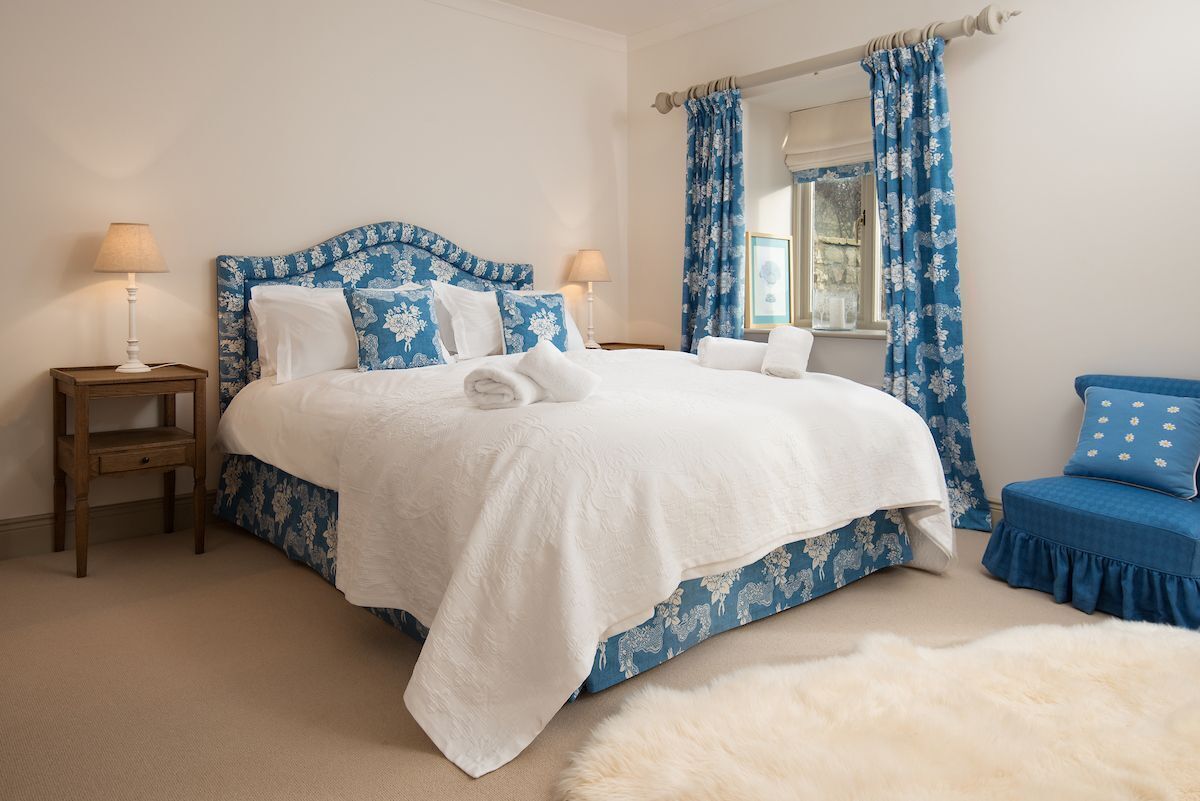 A bedroom with a bed, two bedside tables, a chair, and a window with curtains.
