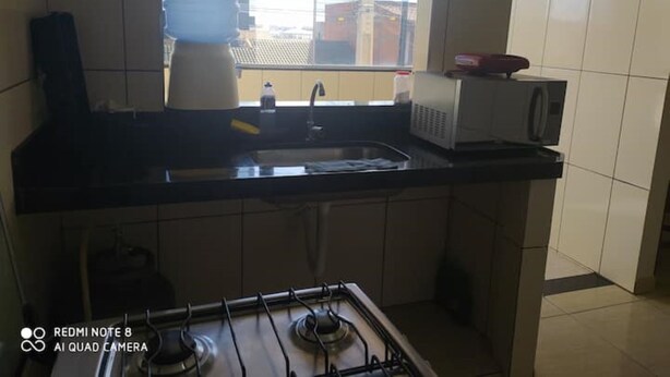 A kitchen with a gas stove, a sink, a microwave, and a window with a view of the outside. - Apartment, Bairro Santa Lúcia, covered garage 2.50x4.70 (Montes Claros)