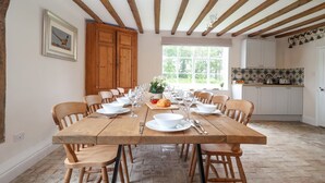 Un espace repas avec une longue table en bois dressée pour le repas, entourée de chaises en bois, et une cuisine en arrière-plan.