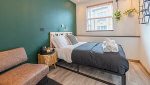 Une chambre à coucher moderne avec un lit, un banc, une table de chevet et une fenêtre avec des stores.