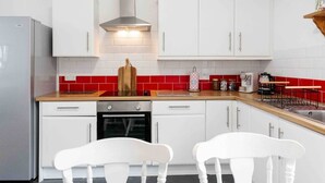 Une cuisine moderne avec des armoires blanches, un pare-feu en carreaux rouges, une hotte de cuisinière en acier inoxydable et un plan de travail en bois.