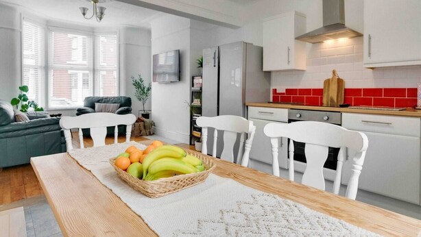 Une cuisine moderne avec des meubles blancs, un pare-feu rouge et un coin repas comprenant une table et des chaises en bois.