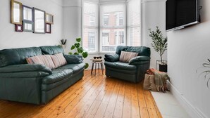 Un salon moderne avec deux canapés en cuir vert, une petite table ronde et une grande fenêtre équipée de stores.