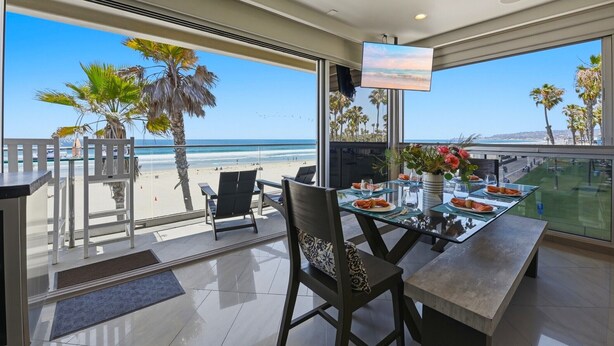 Ein Essbereich mit Blick auf den Strand, einem Flachbildfernseher und einem Balkon mit Geländer.