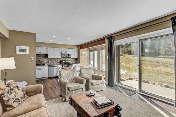 Amplia sala de estar con cocina, asientos cómodos y ventanas grandes con vistas al exterior.