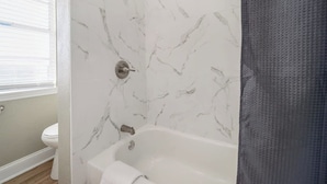 Un baño con pared de mármol, una bañera y un inodoro.