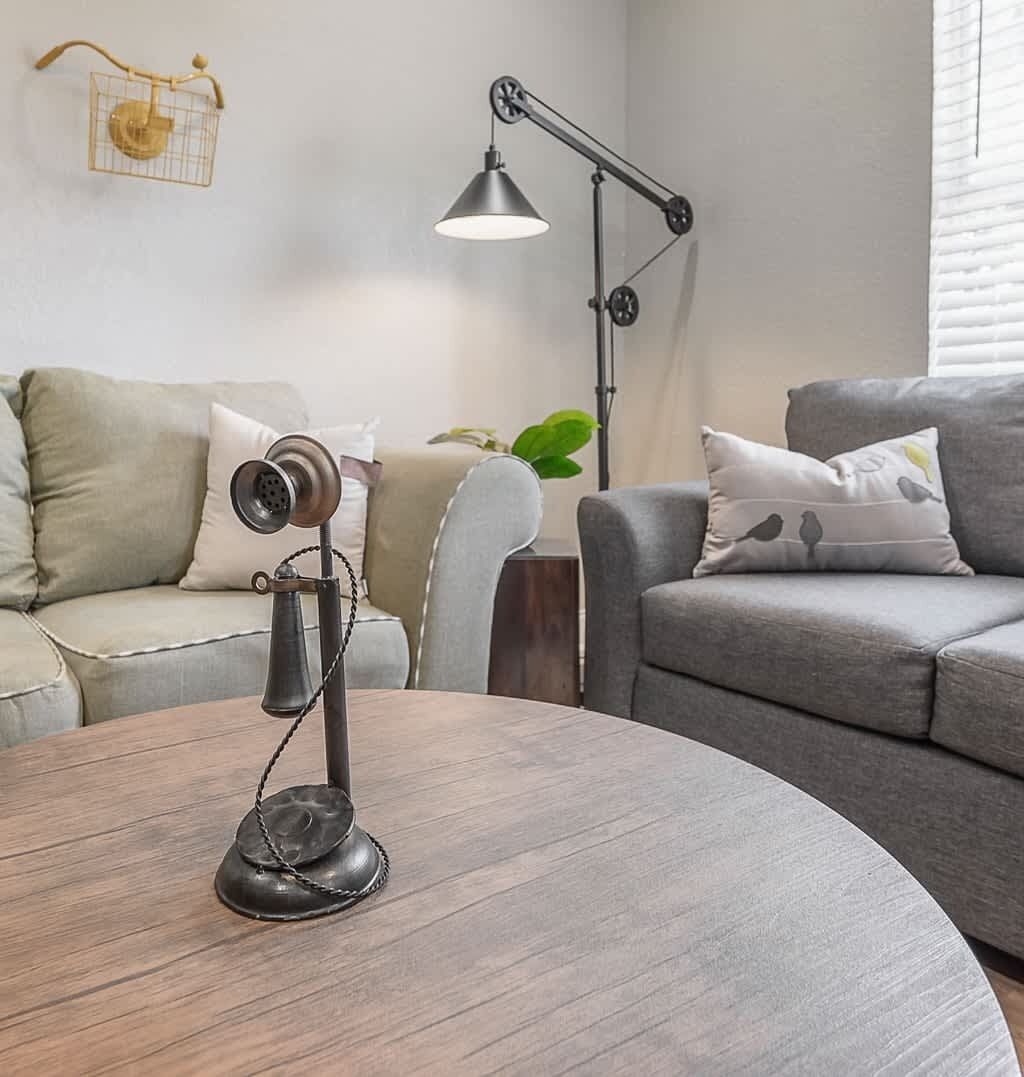 Un salon moderne avec une table basse ronde en bois, deux canapés gris, un lampadaire et un téléphone d’époque.