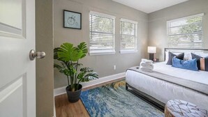 Ein Schlafzimmer mit einem Bett, einer Zimmerpflanze und einem Fenster mit Jalousien.