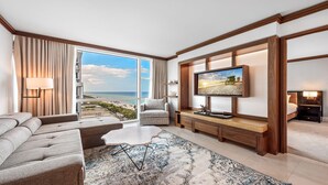 Ein modernes Hotelzimmer mit großem Fenster und Blick auf den Strand, einer bequemen Couch, einem Fernseher und einer kleinen Schreibtischzeile.
