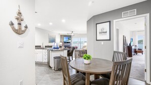 Una cocina moderna con armarios blancos, un comedor con una mesa redonda y sillas, y vistas al exterior.
