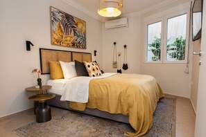 Een slaapkamer met een bed, een nachtkastje, een lamp, een schilderij en een raam.