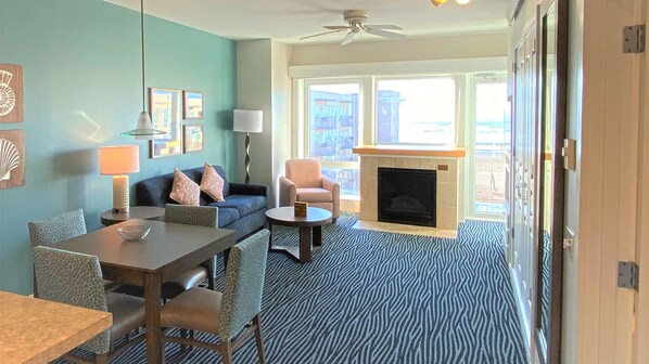 A hotel room with a dining area, a sofa, a fireplace, and large windows.