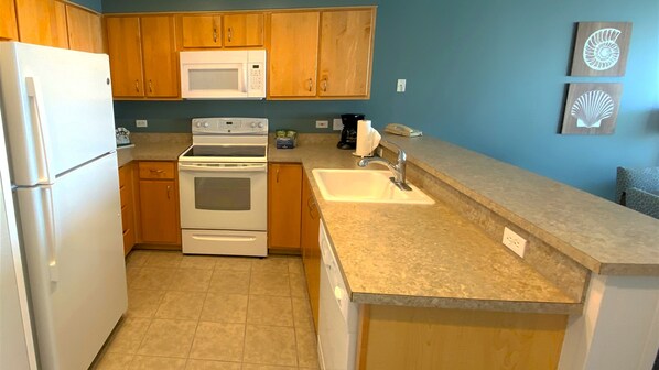 A kitchen with wooden cabinets, a white refrigerator, a microwave, an oven, a sink, and a granite countertop. - Seaside Resort - 1 Bedroom 1 Bath - Assignment 2 (Seaside)