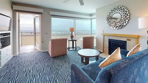 A hotel room with a large window, a sofa, a small table, and a fireplace. - Seaside Resort - Ocean Front 2 Bedroom 2 Bath - Assignment 1 (Seaside)