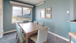 Ein Essbereich mit Tisch und Stühlen, ein Fenster mit Blick auf Gebäude und gerahmte Bilder an der Wand.
